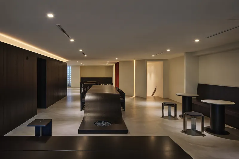 Long view of the dining hall showing the sculptural black counter and glass block window at the rear