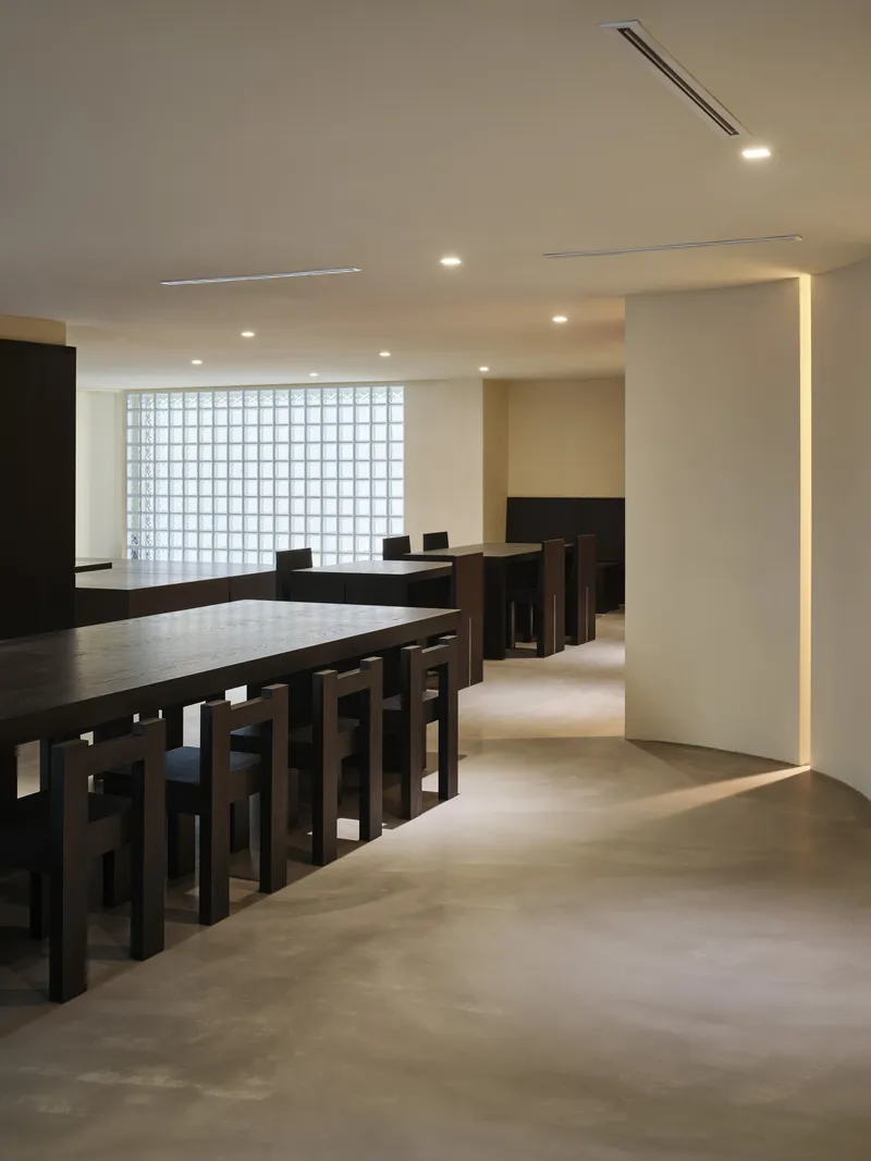 Dark timber dining tables and benches arranged in rows with illuminated vertical slot in the white column