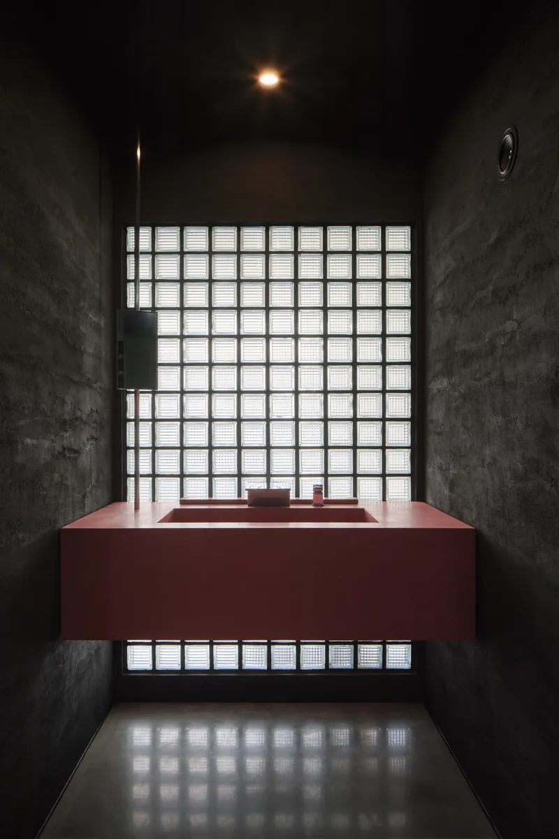 Maroon rectangular basin beneath a glass block window in a dark concrete chamber with reflected light below