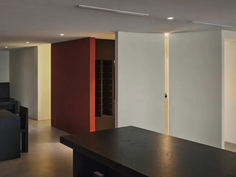 Corner view of the maroon volume and white partitions with edge-lit vertical slots in the ceiling plane