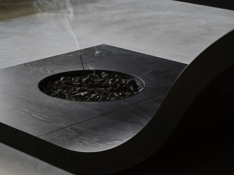 Incense stick burning above black stones in a circular recess on the dark timber surface