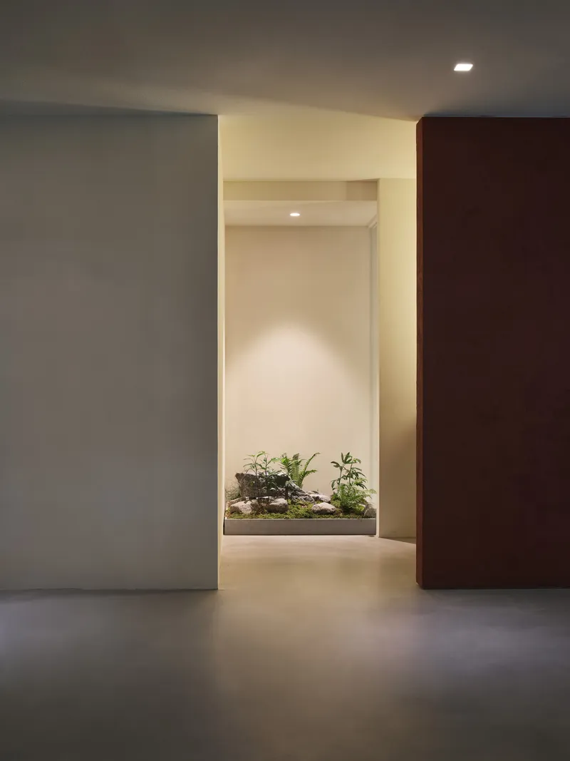 Interior corridor framing a backlit planter niche with small potted plants and grey tiled floor