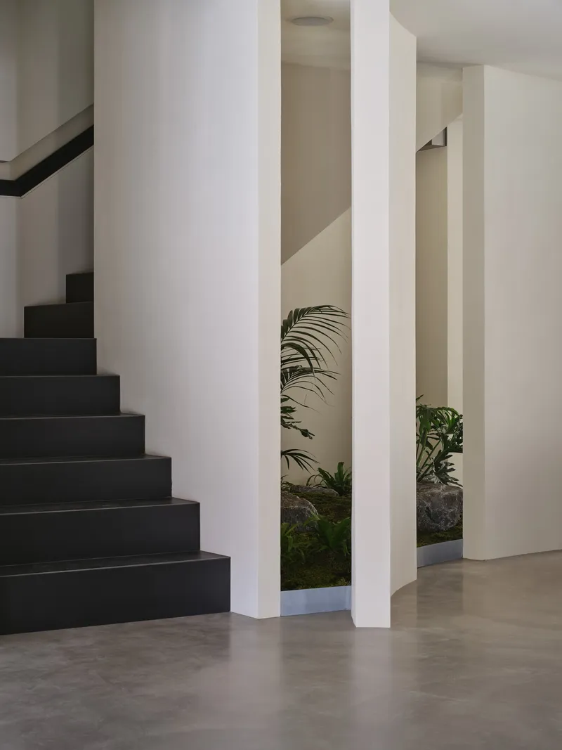 Black staircase alongside white columns framing a planted interior courtyard with palms