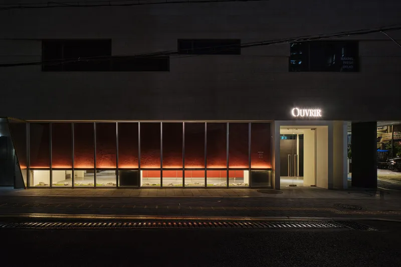 Street facade at night with illuminated red interior visible through vertical glass panels
