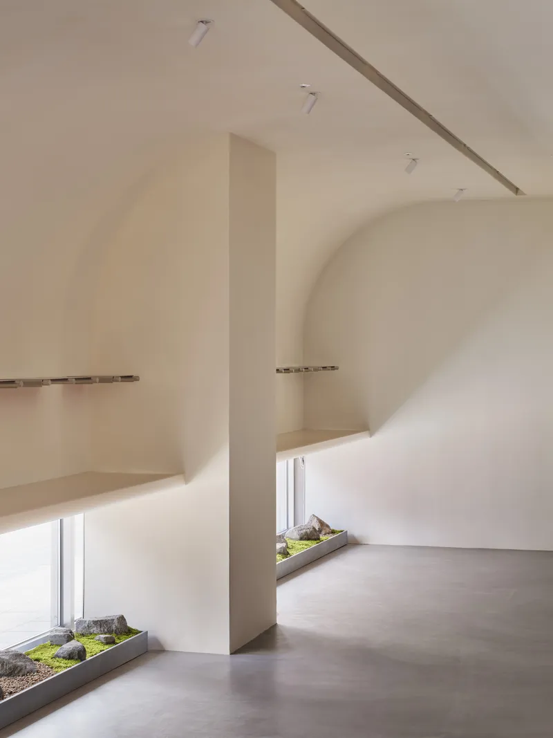 Interior gallery space with vaulted ceiling, polished concrete floor and low planters with moss and stone