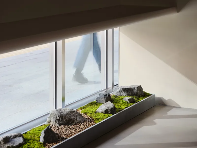 Window planter with moss and rocks as a figure walks past in snow outside