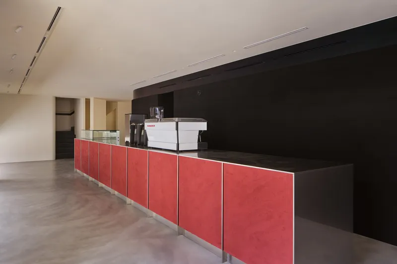 Long service counter with red paneling and black countertop beneath a white vaulted ceiling