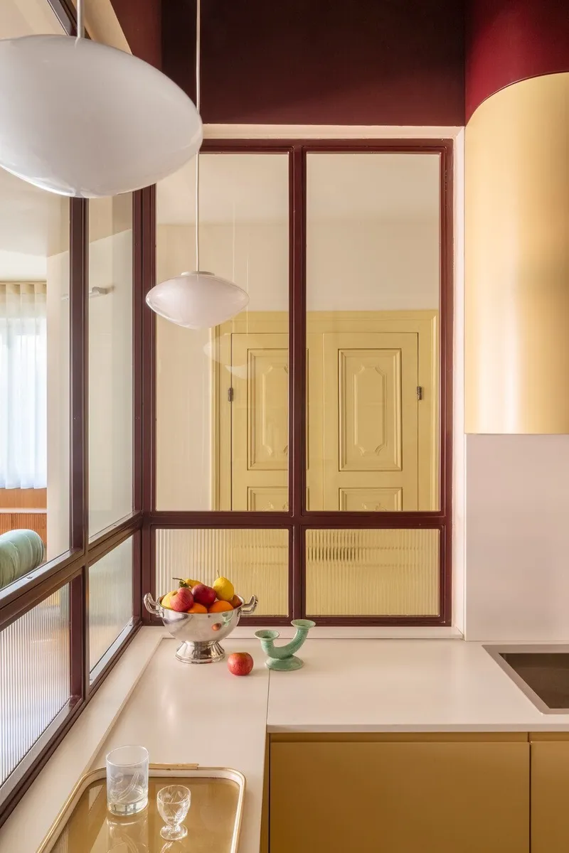 Kitchen counter with pendant light and burgundy-framed glass partition reflecting interior doors