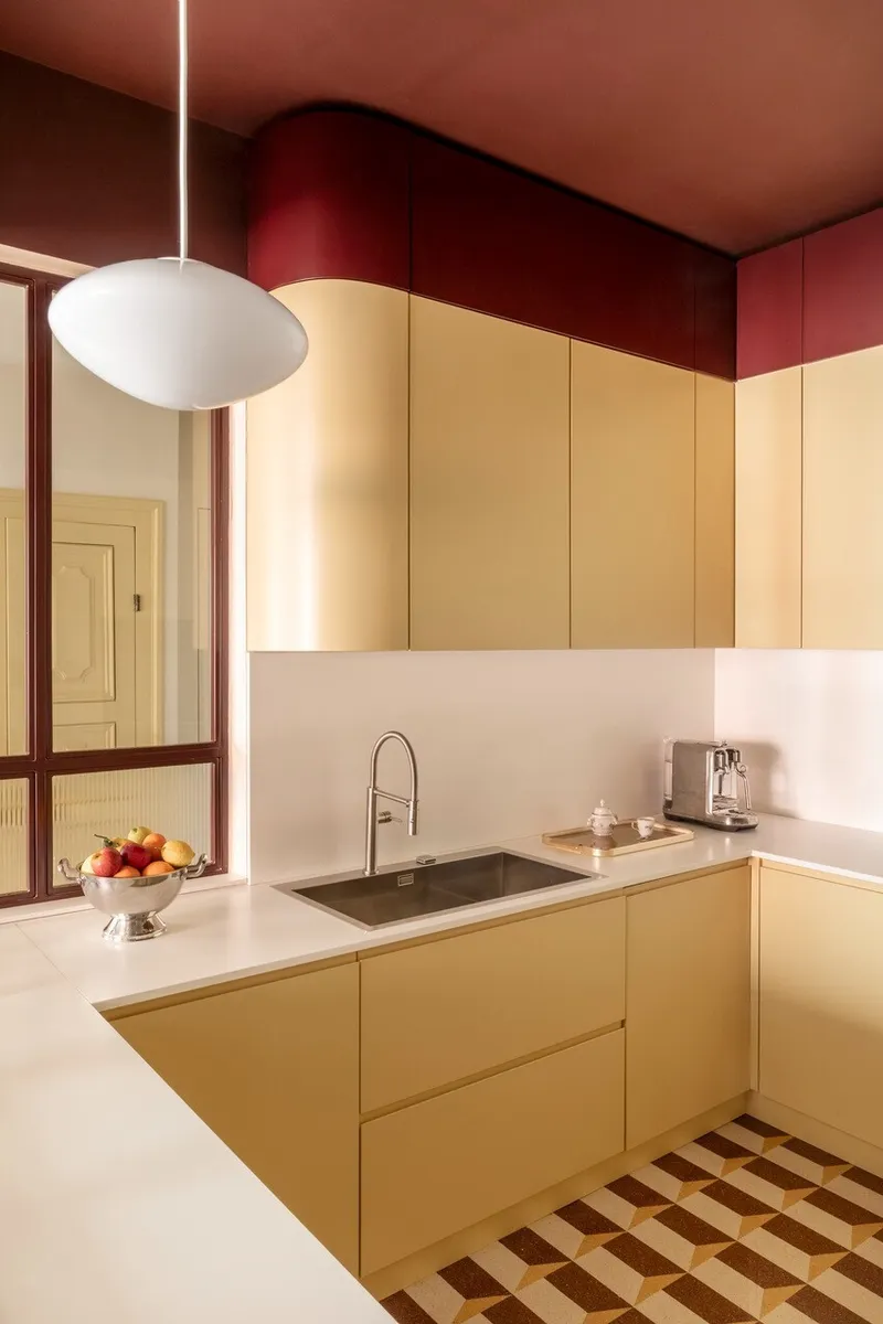 Pale yellow kitchen cabinetry with white countertop beneath a burgundy ceiling and pendant fixture