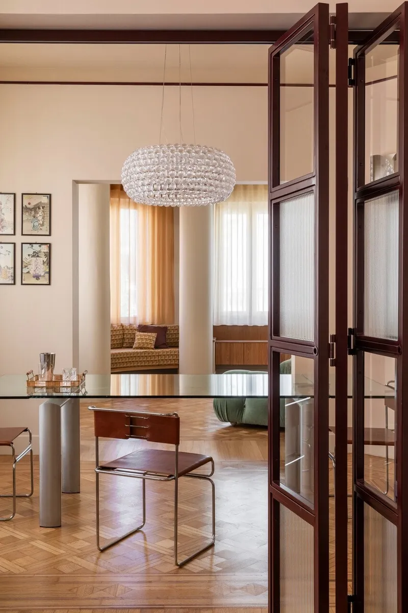 View through folding glass and timber doors into a dining area with a crystal pendant and window seat beyond