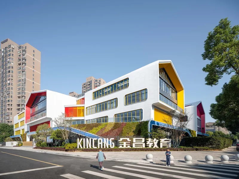 Street view of the white facade with curved forms and colored panels against highrise residential towers