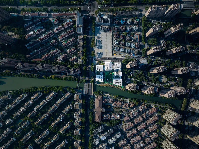 Drone view of the compound surrounded by waterways and tiled-roof residential neighborhoods at midday