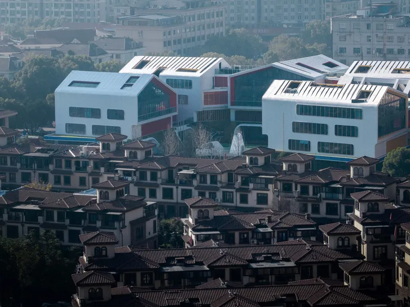 Elevated view of white volumes with louvered roofs rising above a dense neighborhood of tiled-roof houses
