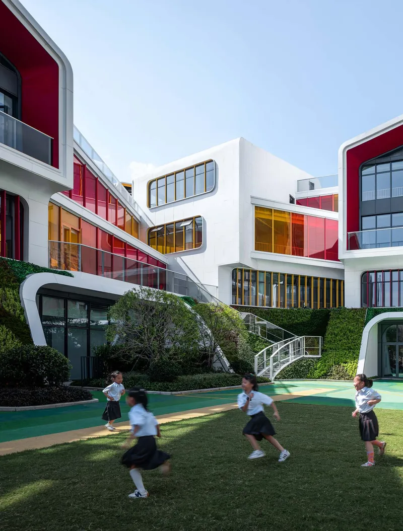 Courtyard with green running track and children playing on lawn below terraced white volumes with glazed facades