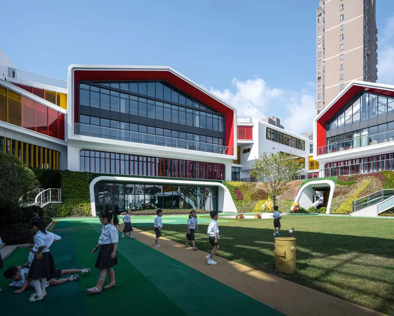 Schoolchildren gathered on the green play track beneath portal-like openings in the white building base