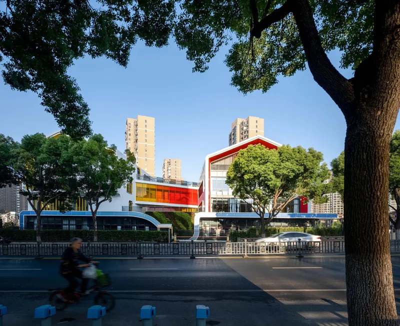 Street view framed by mature trees with a cyclist passing in front of the raised complex