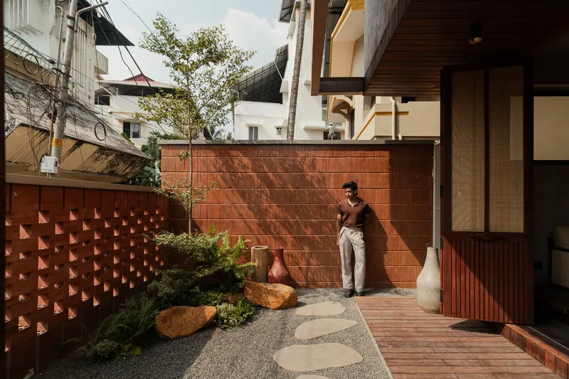 Courtyard garden with red terracotta tile walls, gravel path, boulders, and a person standing by a tree