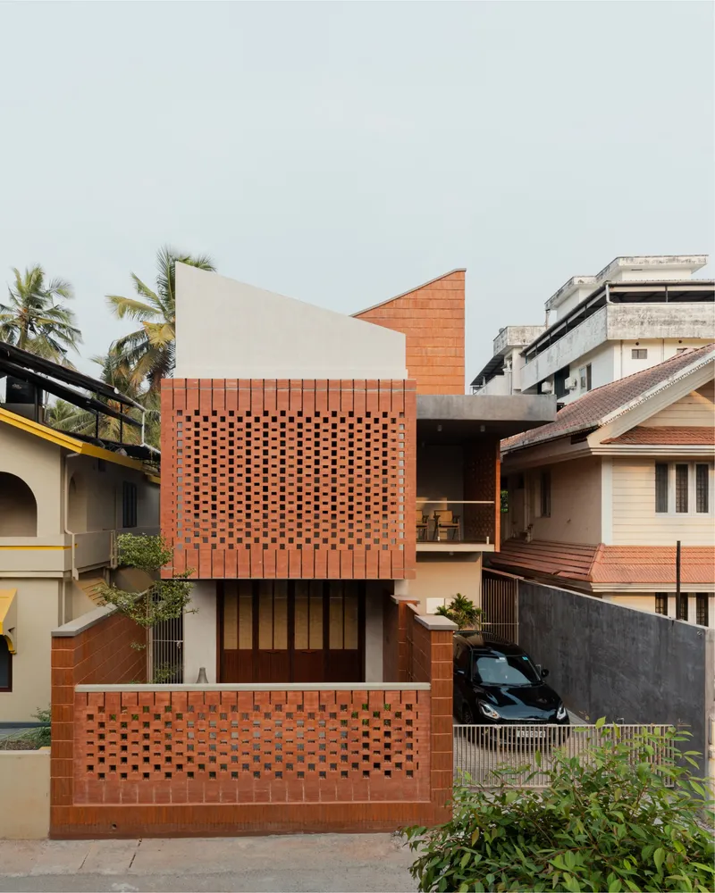 Street facade with perforated red brick screens and white stucco volumes between neighboring houses