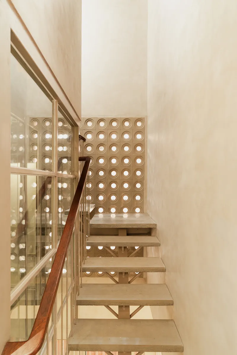 Timber staircase with glass balustrade and circular perforated screen wall in a skylit stairwell