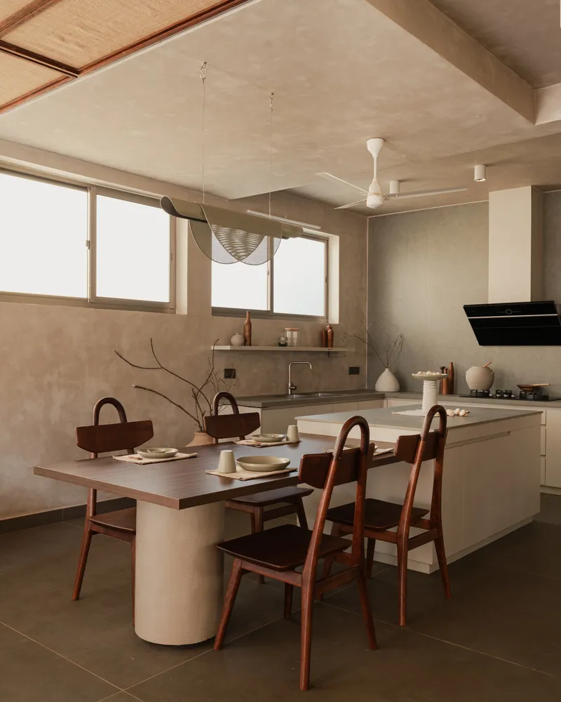 Open kitchen and dining area with cylindrical plaster table base beneath sliding frosted glass windows