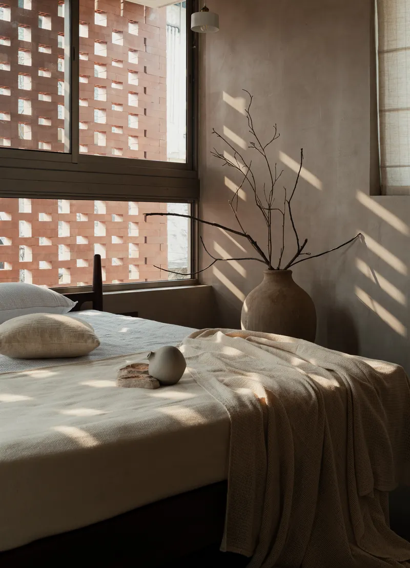 Bedroom window with chequered brick screen casting dappled shadows across the bed