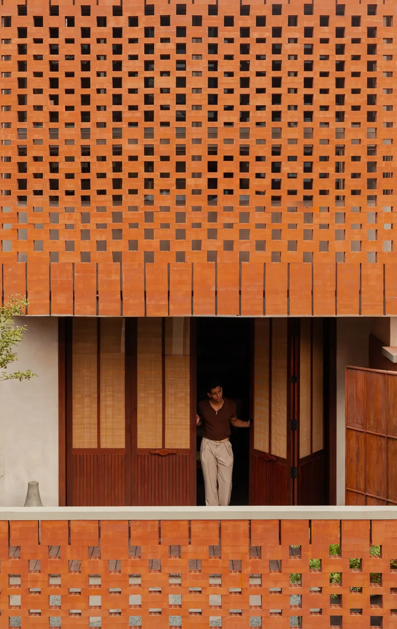 Perforated terracotta brick facade with a person standing in the recessed timber doorway