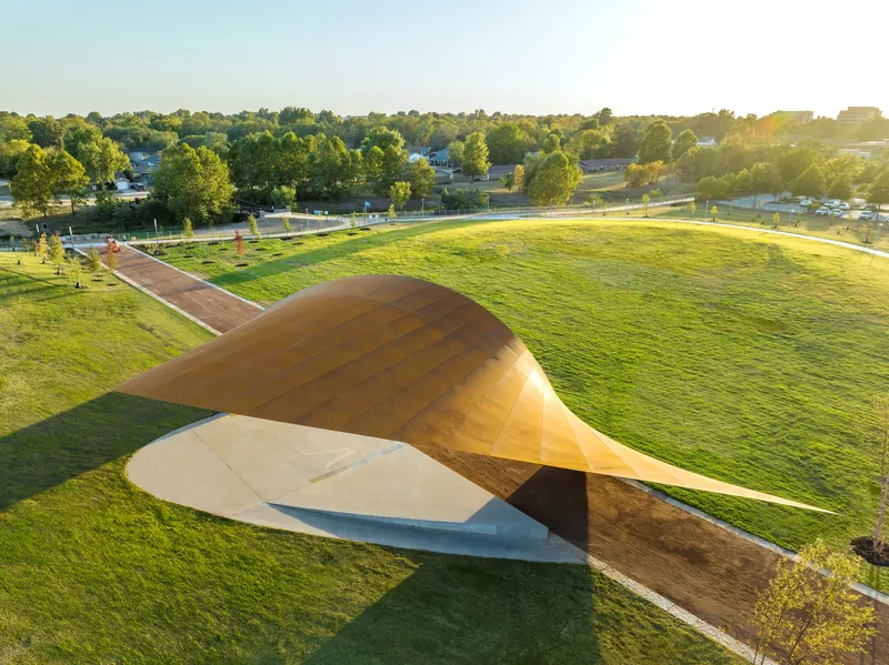 Aerial view of the curved wood shell pavilion rising from a concrete base in evening light