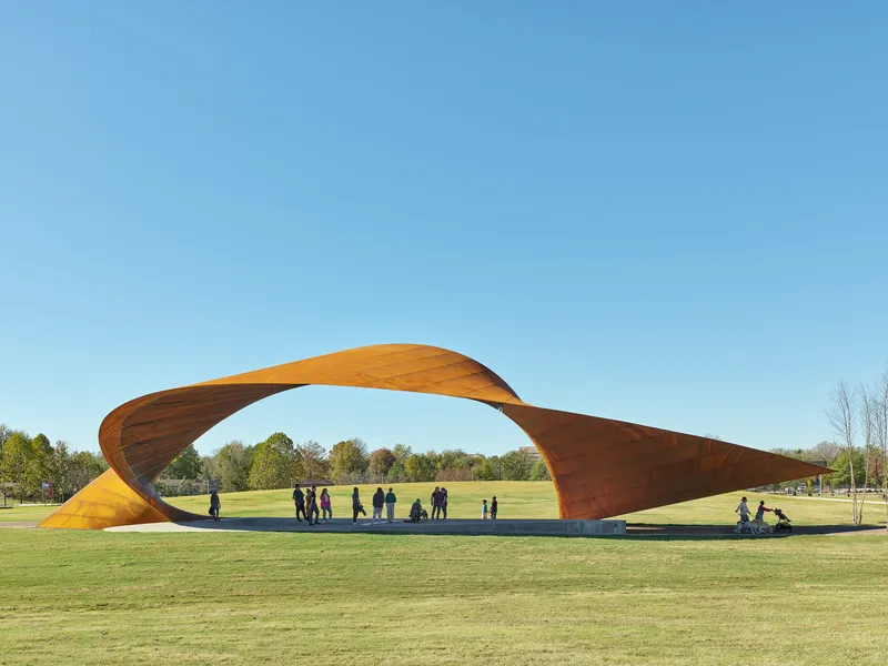 Twisted weathering steel canopy spanning a lawn with visitors gathered beneath on a clear afternoon