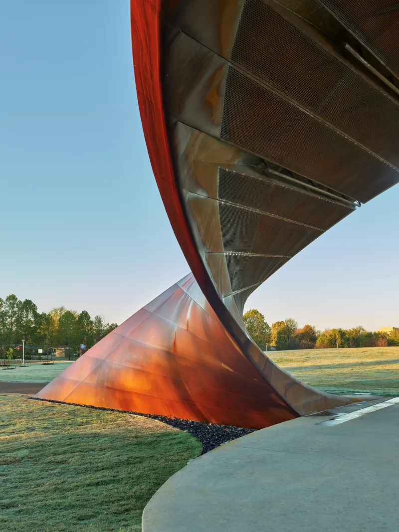 Close view of the twisted steel support column meeting the perforated metal soffit at dawn
