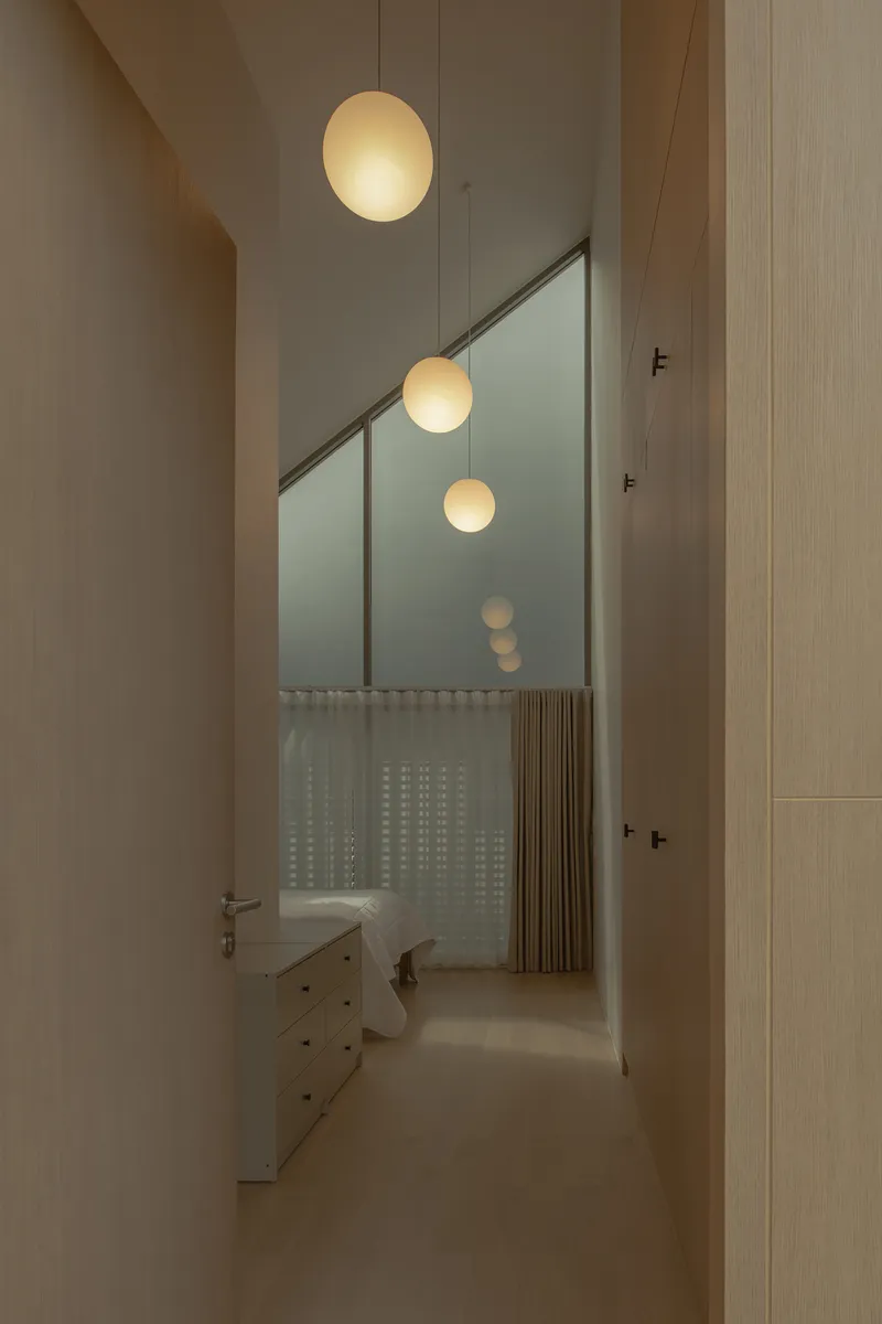 Corridor view through angled glass partition with suspended globe pendants and translucent curtain