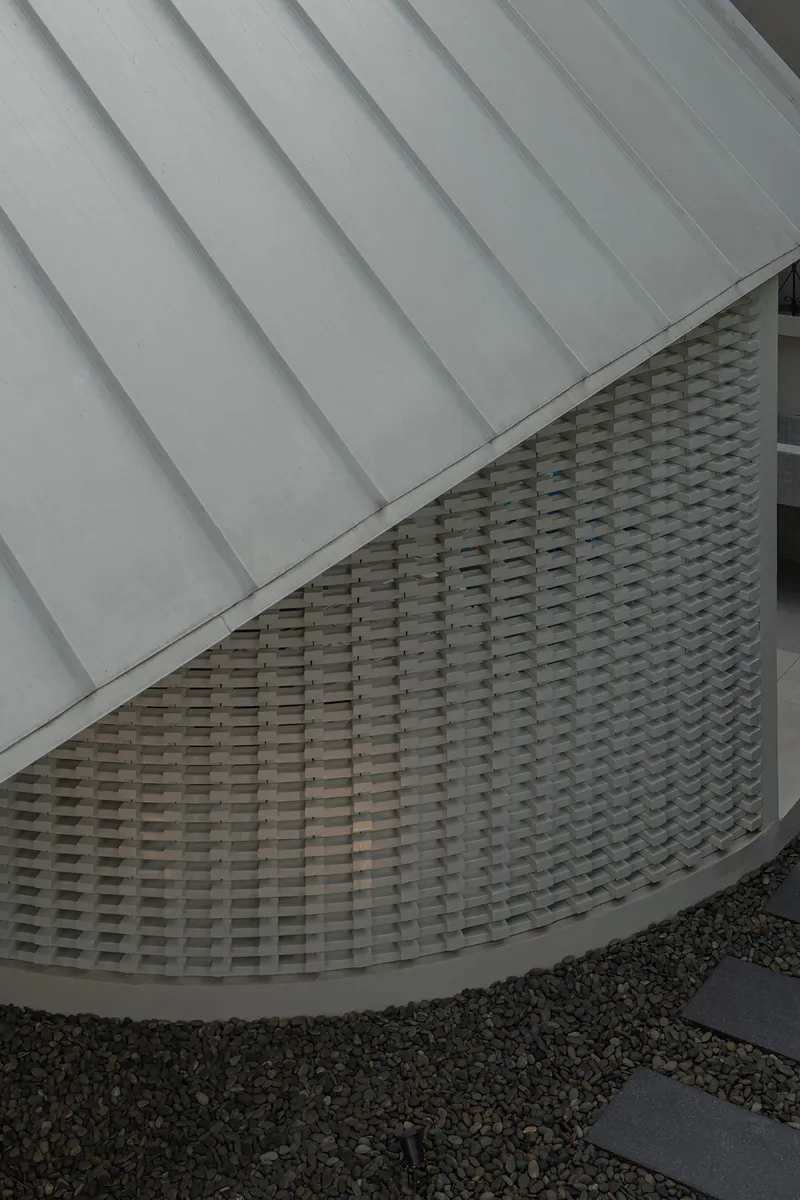 Detail of curved woven brick facade beneath metal standing seam roof and gravel courtyard