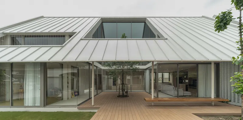 Timber deck courtyard enclosed by glass-walled volumes beneath a sloping white metal roof with skylight