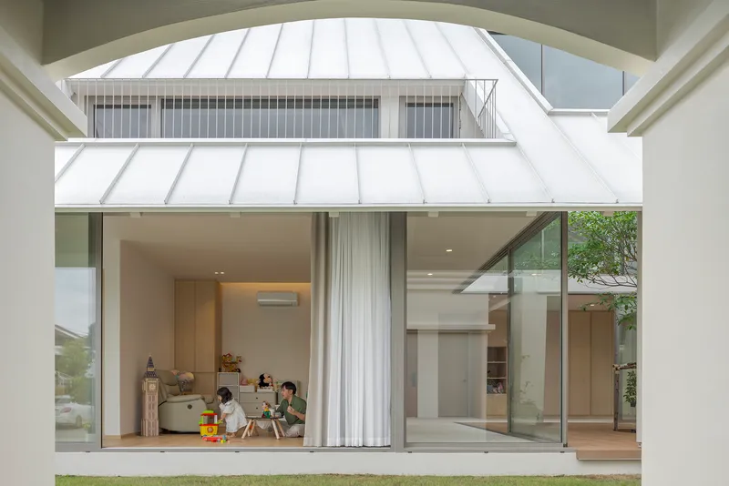 View across lawn to glazed living area with children playing and metal roof overhead
