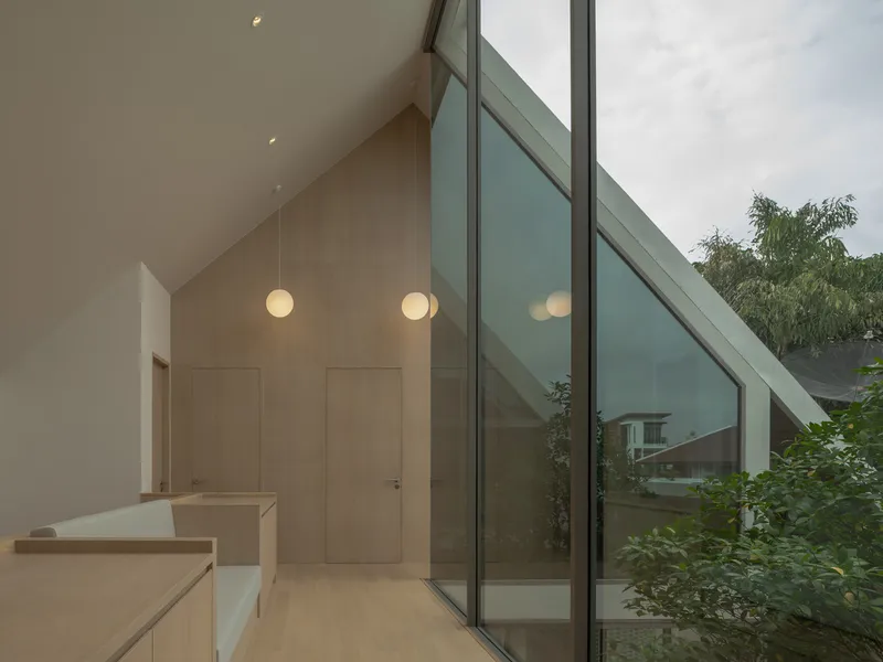 Interior hallway with sloped glazing, pendant lights, and pale wood cabinetry at dusk