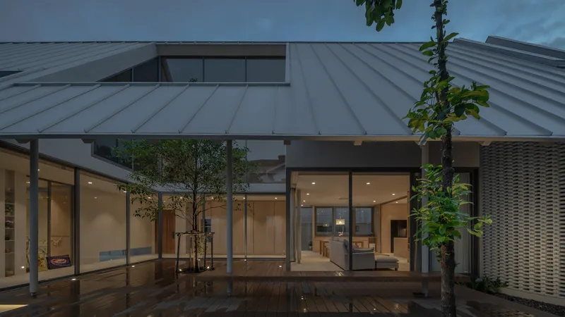 Courtyard terrace with timber deck and planted trees enclosed by glass walls beneath a standing seam metal roof