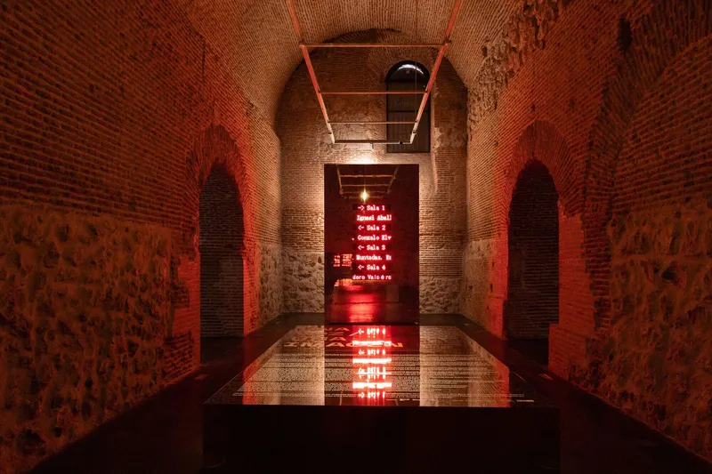 Vaulted brick corridor with red LED signage reflected in a water channel running down the center