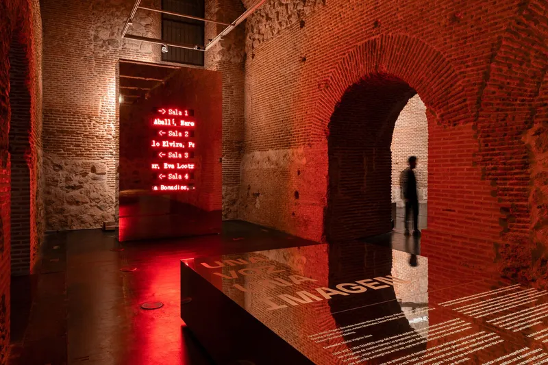 Brick archway framing a visitor standing in red light beside a reflective floor panel