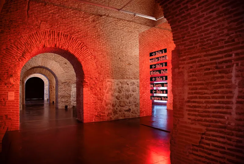Sequence of brick arches receding through red-lit chambers with stone and brick walls
