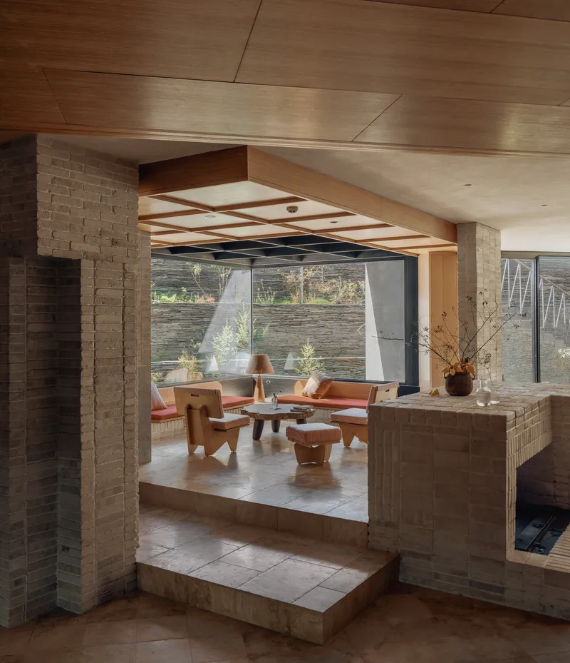 Sunken living area framed by brick columns and timber ceiling beams with glazed walls beyond