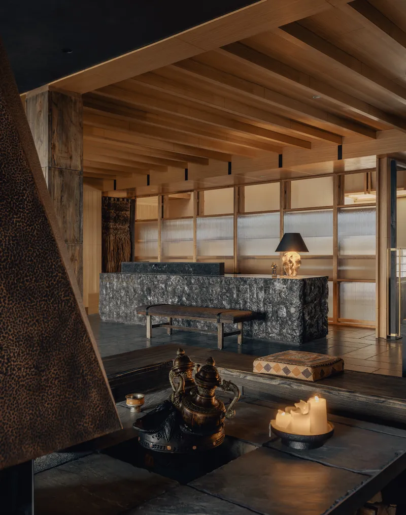 Stone-clad reception desk with timber ceiling beams and translucent wall panels at dusk