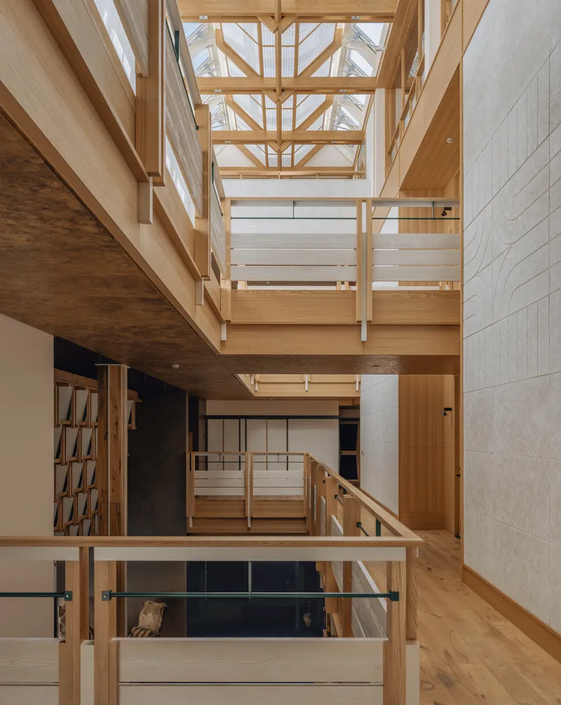 Multi-level timber interior atrium with exposed beams, walkways, and a skylight above