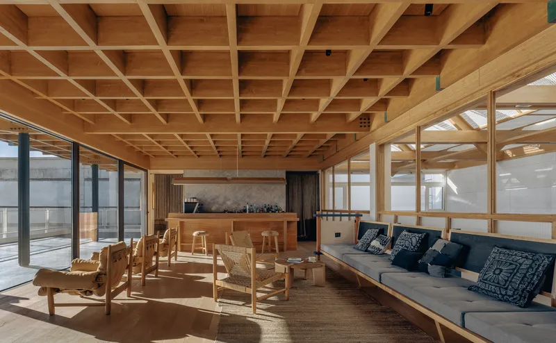 Communal lounge with exposed timber coffered ceiling and glazed walls overlooking a terrace