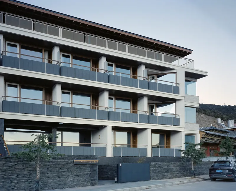 Street facade showing three-story elevation with continuous balconies and dark stone base wall at dusk