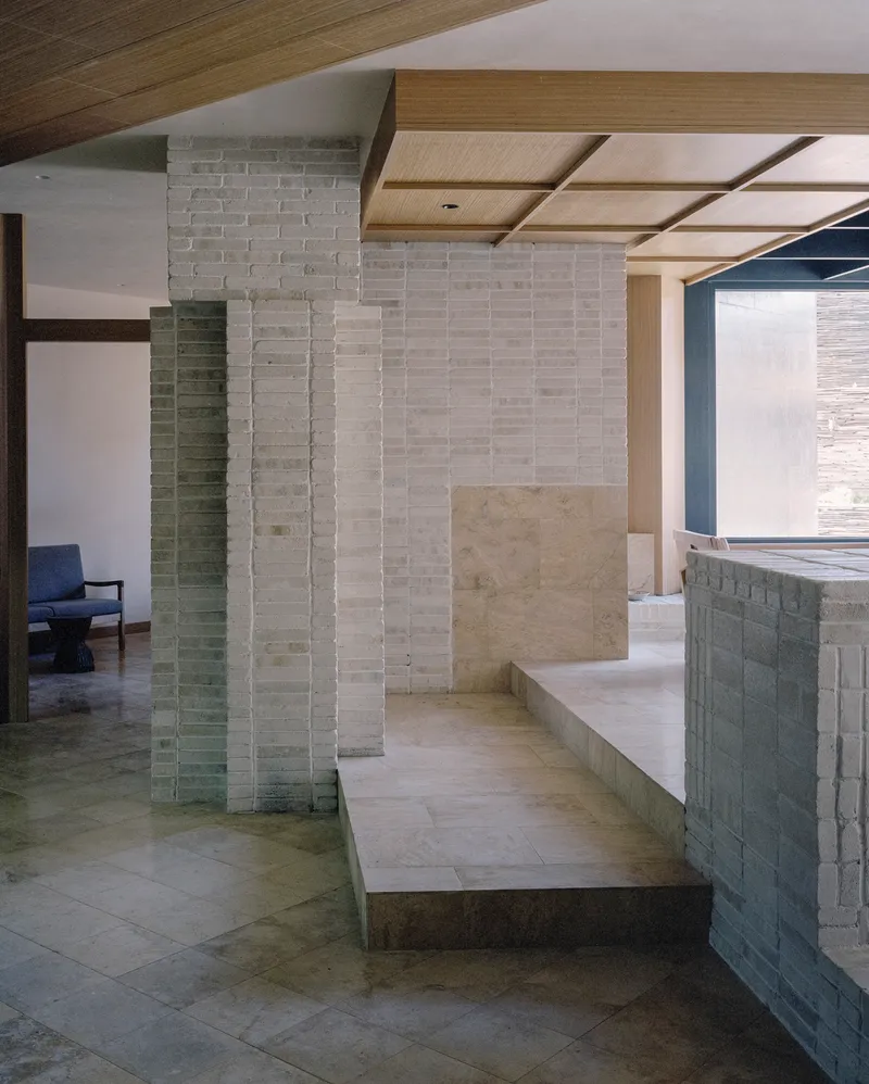 Stepped brick platforms and columns forming seating areas under a coffered timber ceiling