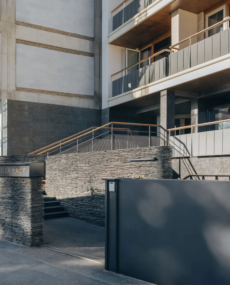 Entrance stairway with horizontally stacked stone walls and metal handrail in afternoon sunlight