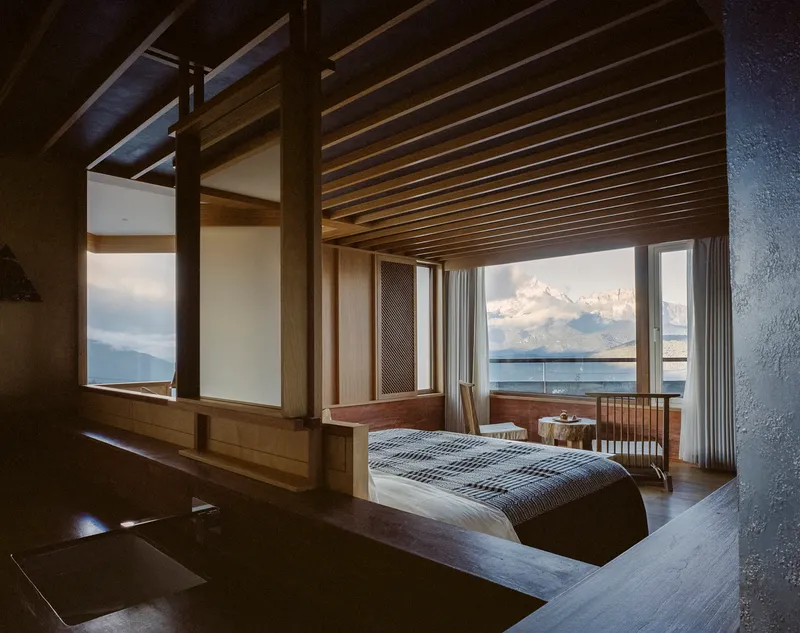 Bedroom with exposed timber beams and full-height windows facing distant clouds and lake