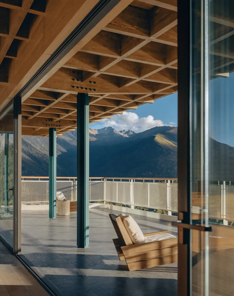 Covered terrace with timber grid ceiling and steel columns framing snow-capped mountains beyond