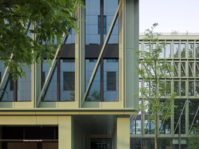 Facade detail showing diagonal yellow bracing columns and young street trees against a white sky