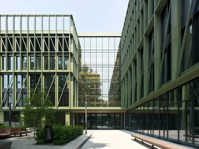 Glass skybridge connecting two wings with diagonal bracing over a courtyard entry and wooden benches