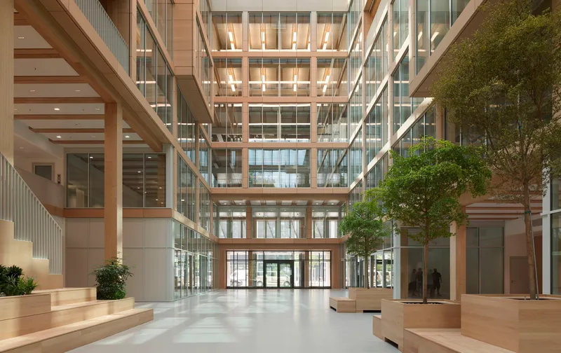 Glazed atrium with timber-lined balconies and a planted tree centered on the polished floor